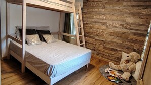 A bunk bed with a ladder, a wooden floor, a stone wall, and a teddy bear on a small rug.