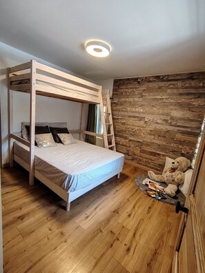 A bunk bed with a ladder, a wooden floor, a stone wall, and a teddy bear on a small rug.