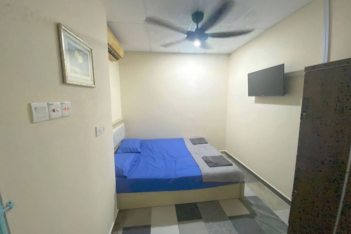 A small, single-bed room with a ceiling fan, a mounted TV, and a checkered floor.