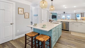 A modern kitchen with a central island, bar stools, pendant lighting, and a view to the dining area. - Huge renovated townhome, sleeps 11, beach-side of 98 with gorgeous beach access (Me)