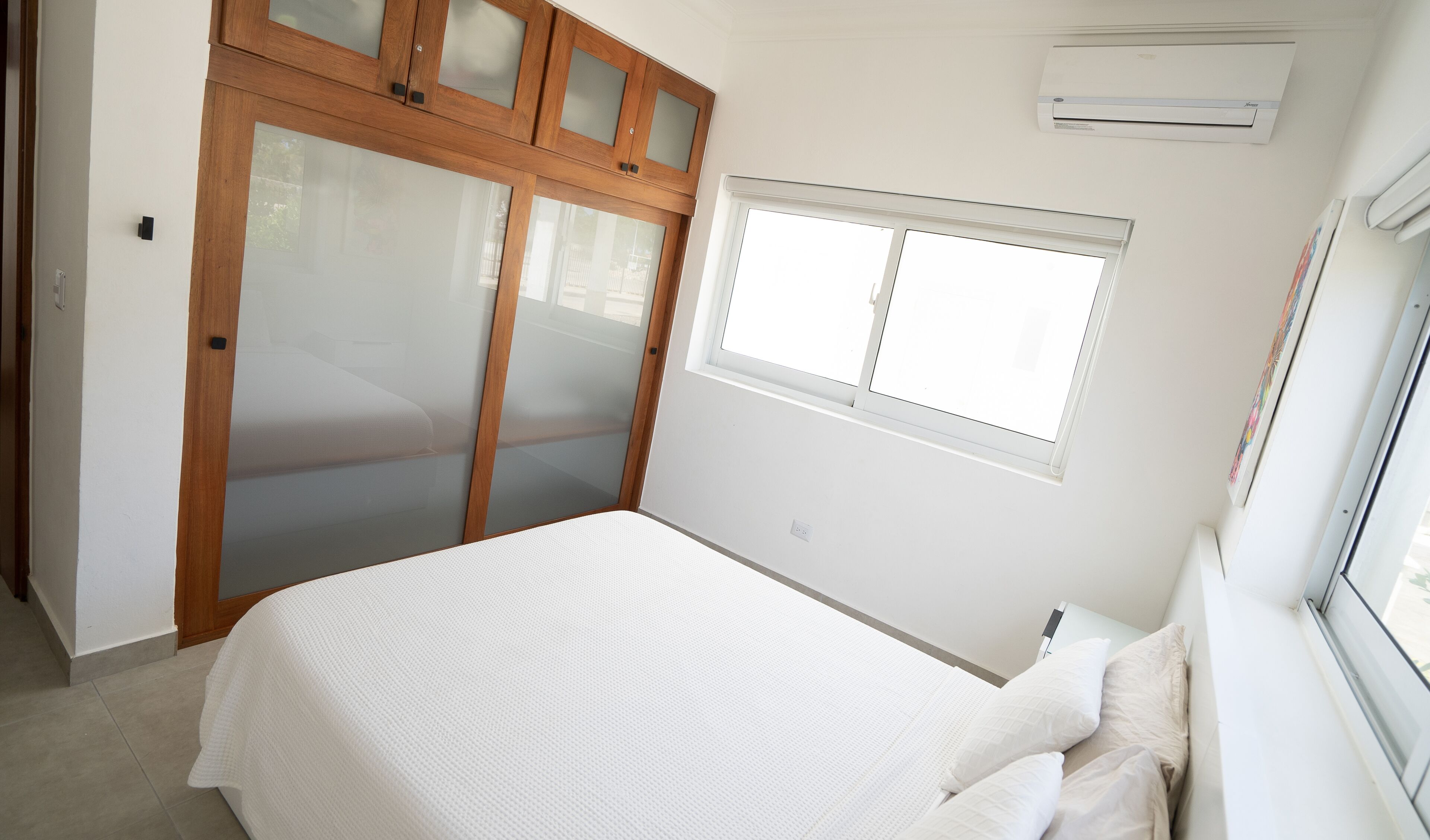 A bedroom with a bed, a window, and a wardrobe with frosted glass doors.