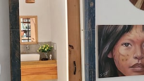 A room with a wooden door, a white sink, a mirror, and a painting on the wall.