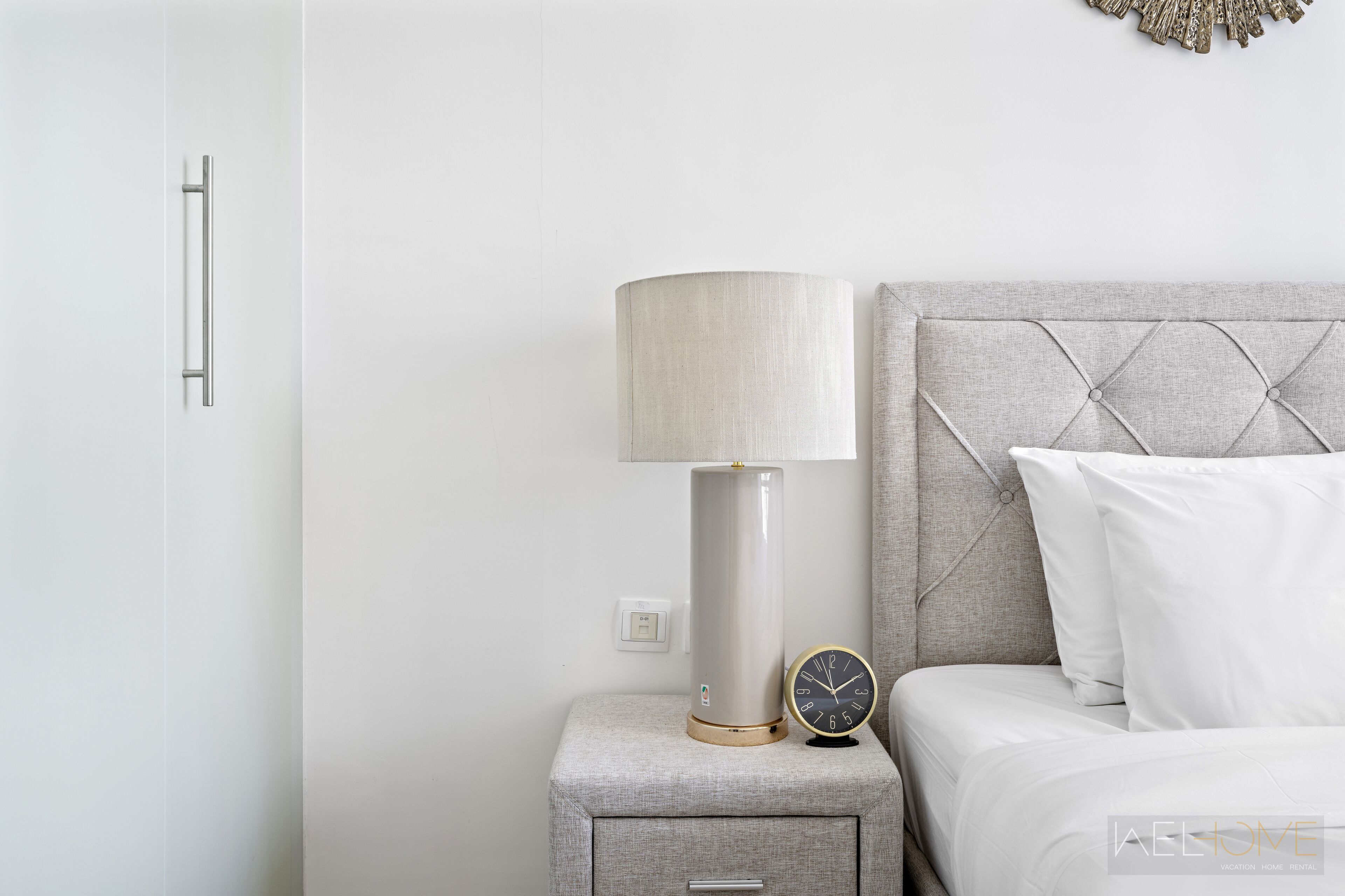 Een moderne slaapkamer met nachtkastje, lamp, klok en bed met een gestuufd hoofdeinde.
