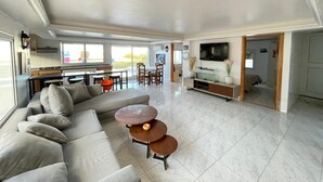 A spacious living area with a sofa, a coffee table, and a TV. There is a kitchen area with a dining table and chairs. - Dar Riahi Ras Jbal (Ras Jebel)