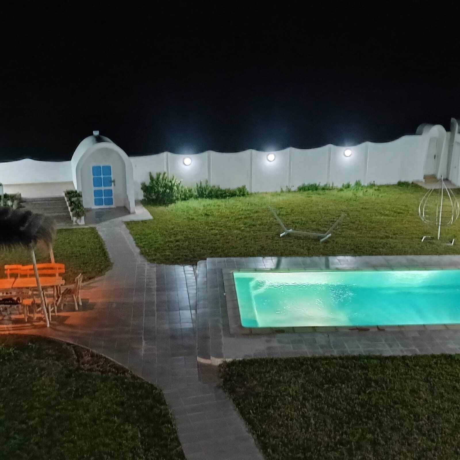 A nighttime view of a swimming pool area with a small building, a bench, and a pathway.