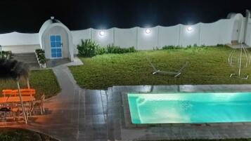A nighttime view of a swimming pool area with a small building, a bench, and a pathway.