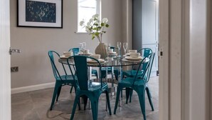 A dining area with teal chairs, a glass table, and a vase with flowers.