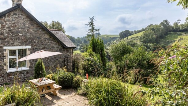 A stone cottage with a small patio, a table, and an umbrella.