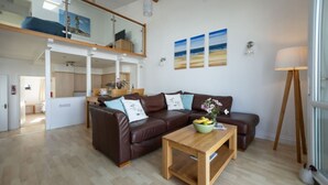 A spacious living room with a brown leather sofa, a wooden coffee table, and a dining area in the background. - 2 Bed Beach House in a fantastic sea front setting (Westward Ho!)