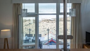 A room with a large window overlooking a beach, a lamp, and a television. - 2 Bed Beach House in a fantastic sea front setting (Westward Ho!)