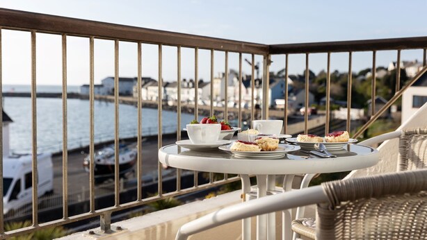 Un balcón con una mesa dispuesta para tomar té, con vistas a un puerto con barcos y edificios.