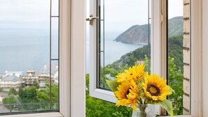 Una ventana con vista a un paisaje costero, un jarrón con girasoles y un picaporte.