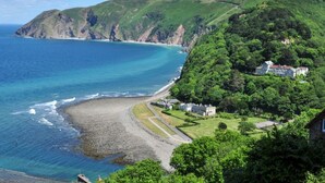 Un paisaje costero con playa, un acantilado y una zona residencial con casas.