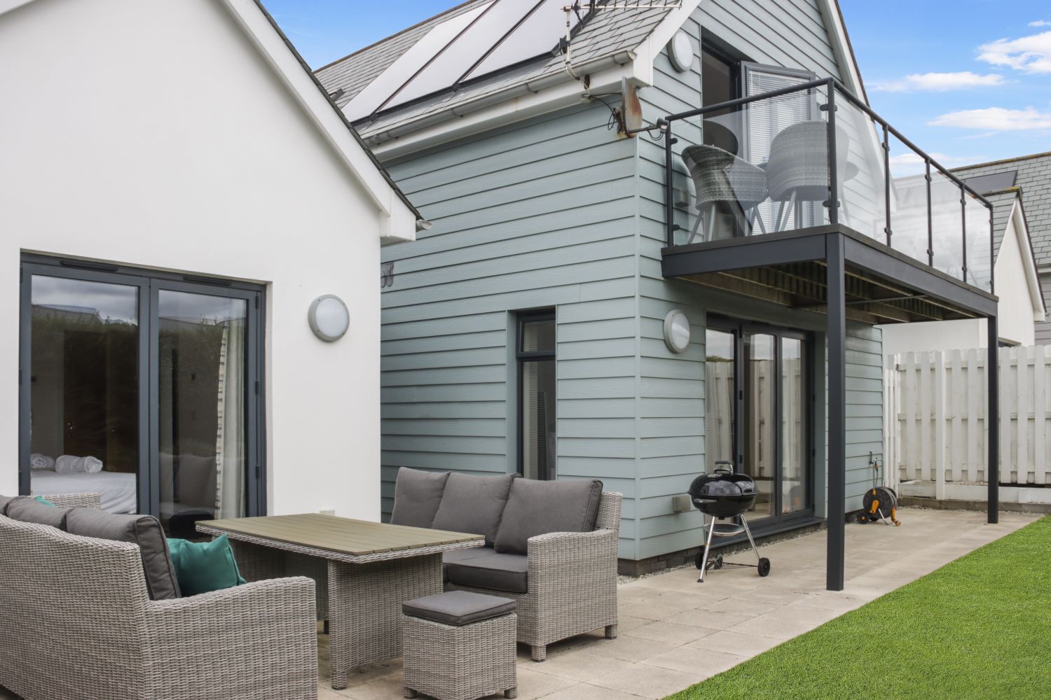Una casa moderna con patio, mobiliario exterior y una parrilla.