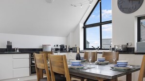 Une cuisine moderne avec un coin repas, comprenant une grande fenêtre, une horloge et une table à manger dressée pour quatre personnes.