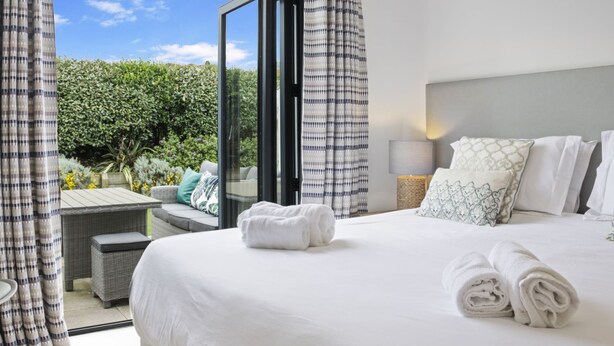 Une chambre d’hôtel avec un grand lit, une petite table et une vue sur un jardin, visible à travers une porte vitrée.