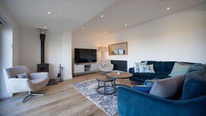 A modern living room with a blue sofa, a white armchair, a round coffee table, and a fireplace. - Stylish beachside house with superb coastal views (Westward Ho!)