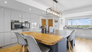 A modern kitchen with a central island, stainless steel appliances, and a view to the outside. - Stylish beachside house with superb coastal views (Westward Ho!)