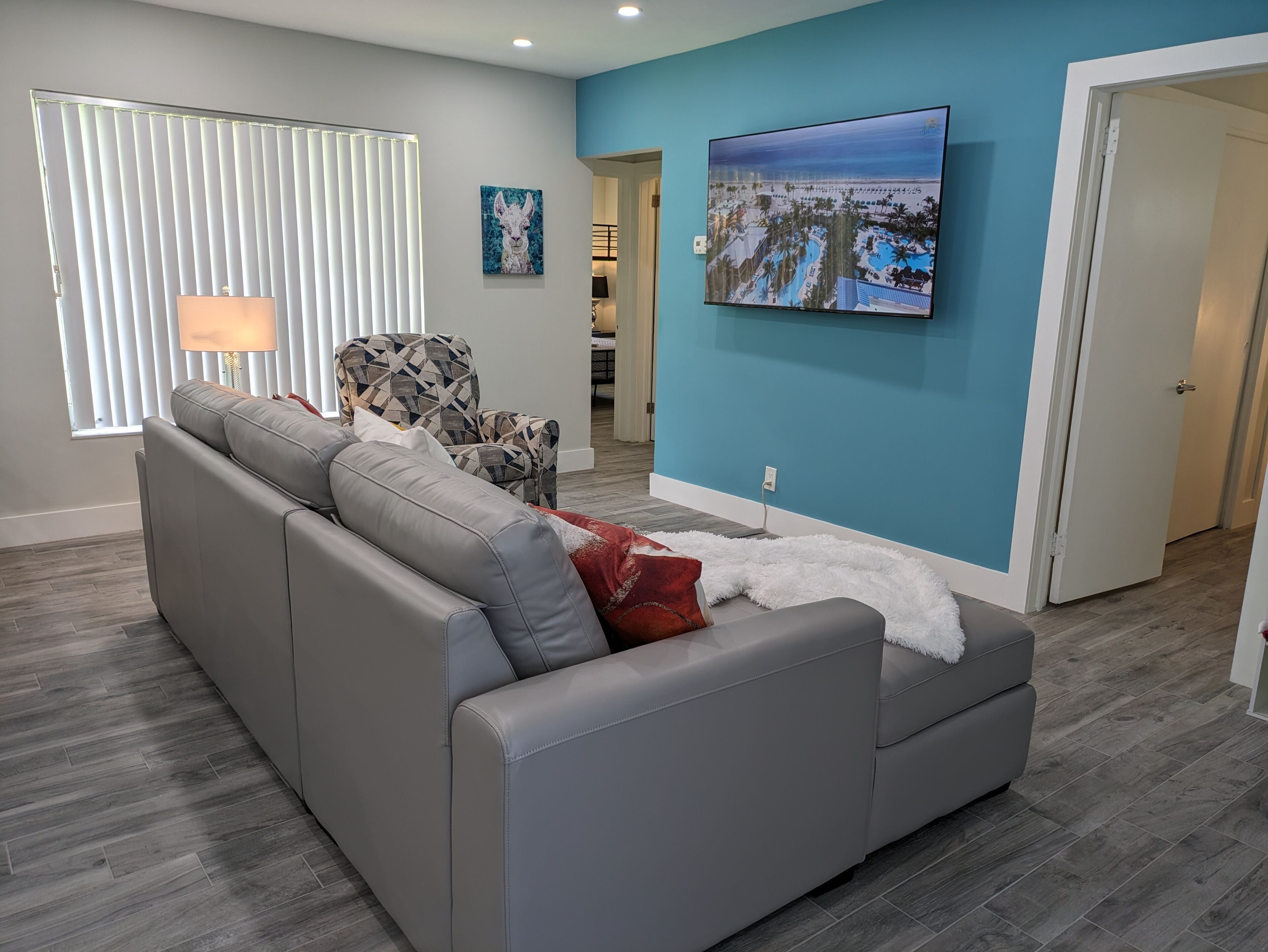 A modern living room with a grey sectional sofa, a patterned armchair, and a large TV on a blue wall.