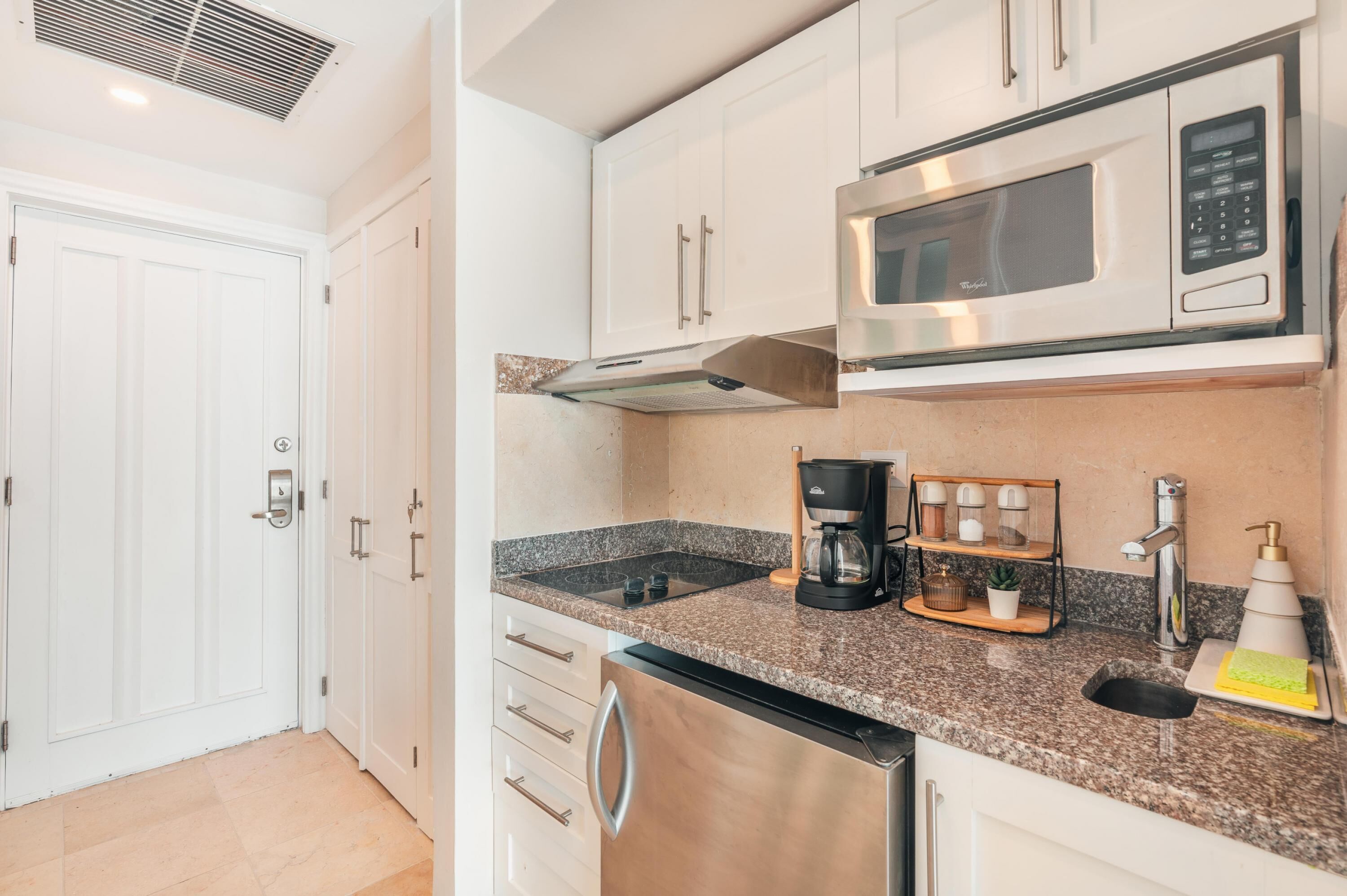 A compact kitchen with white cabinets, a stainless steel microwave, a coffee maker, and a sink.
