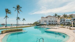 A resort pool with a clear blue water feature, surrounded by palm trees and a beachfront view. - Modern Studio With Ocean View in Punta Palmera (Punta Cana)