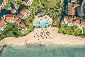 Vista aérea de un complejo turístico con una piscina central, varias villas y acceso a la playa.