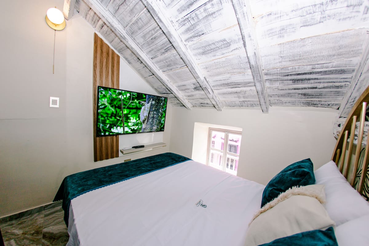Ein Schlafzimmer mit einem Bett, einem an der Wand montierten Fernseher und einem Fenster.