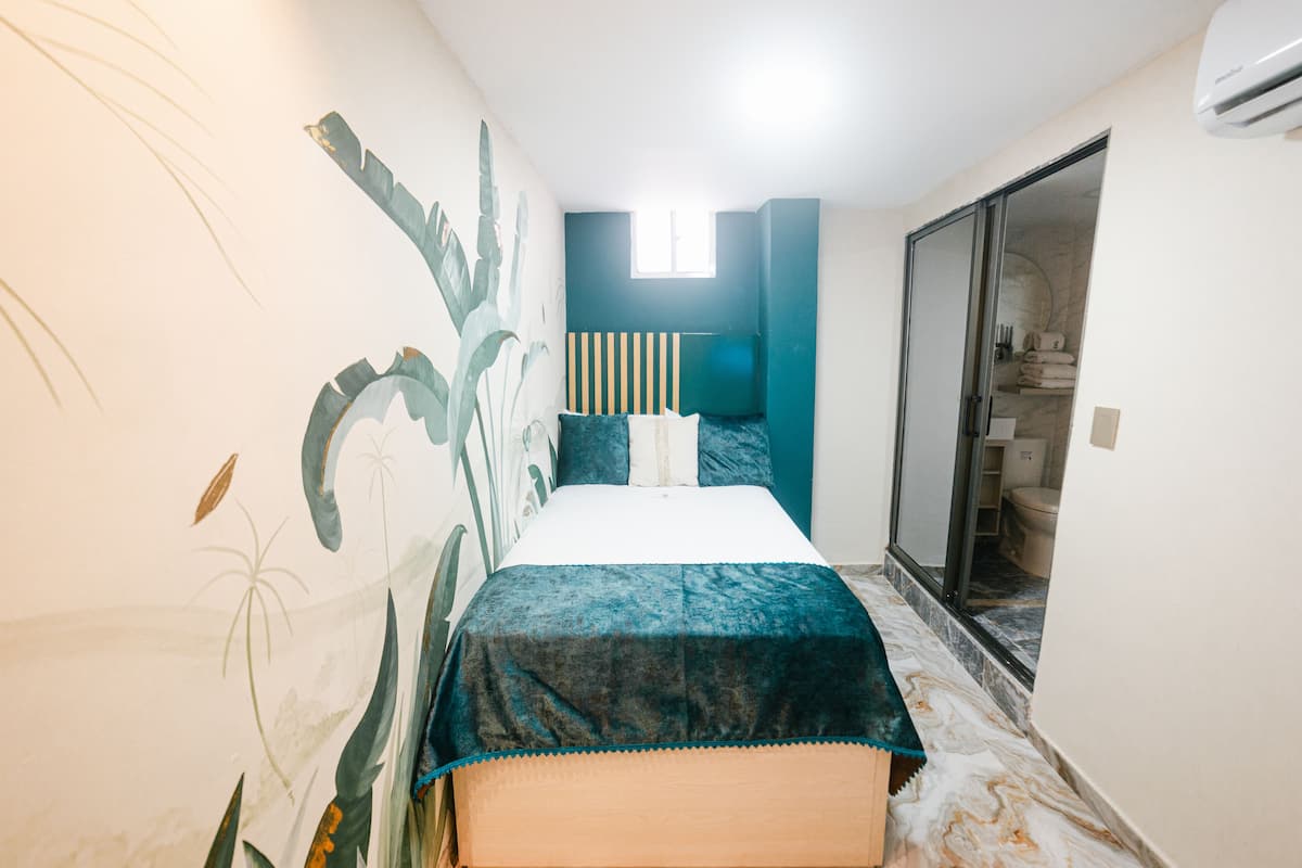 Ein Schlafzimmer mit Bett, Fenster und einem durchgehenden Türspalte sichtbaren Badezimmer.