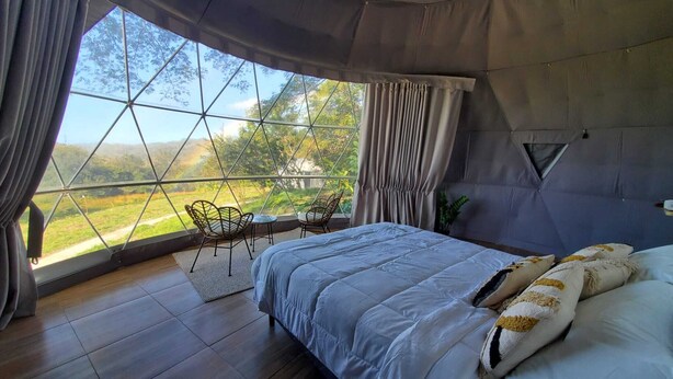 A bedroom with a large window, a bed, and a small table with chairs. - Vida Aventura Glamping Deluxe Dome (Bagaces)