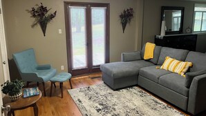 Una sala de estar con un sofá seccional gris, un sillón azul, una mesita con un libro y una alfombra estampada.