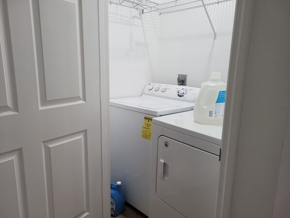 Un cuarto de lavandería con lavadora, secadora y botellas de detergente.
