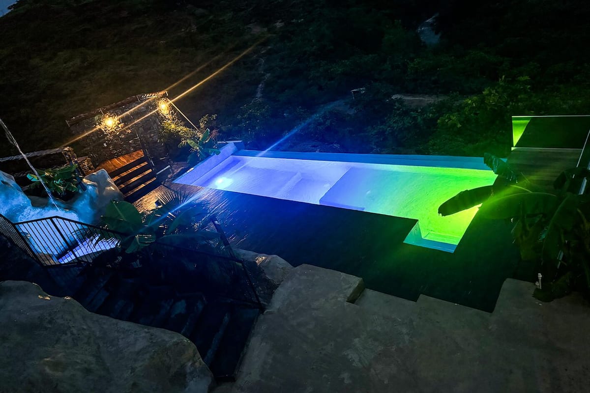 Une piscine agrémentée d’une cascade, entourée de rochers et de végétation.