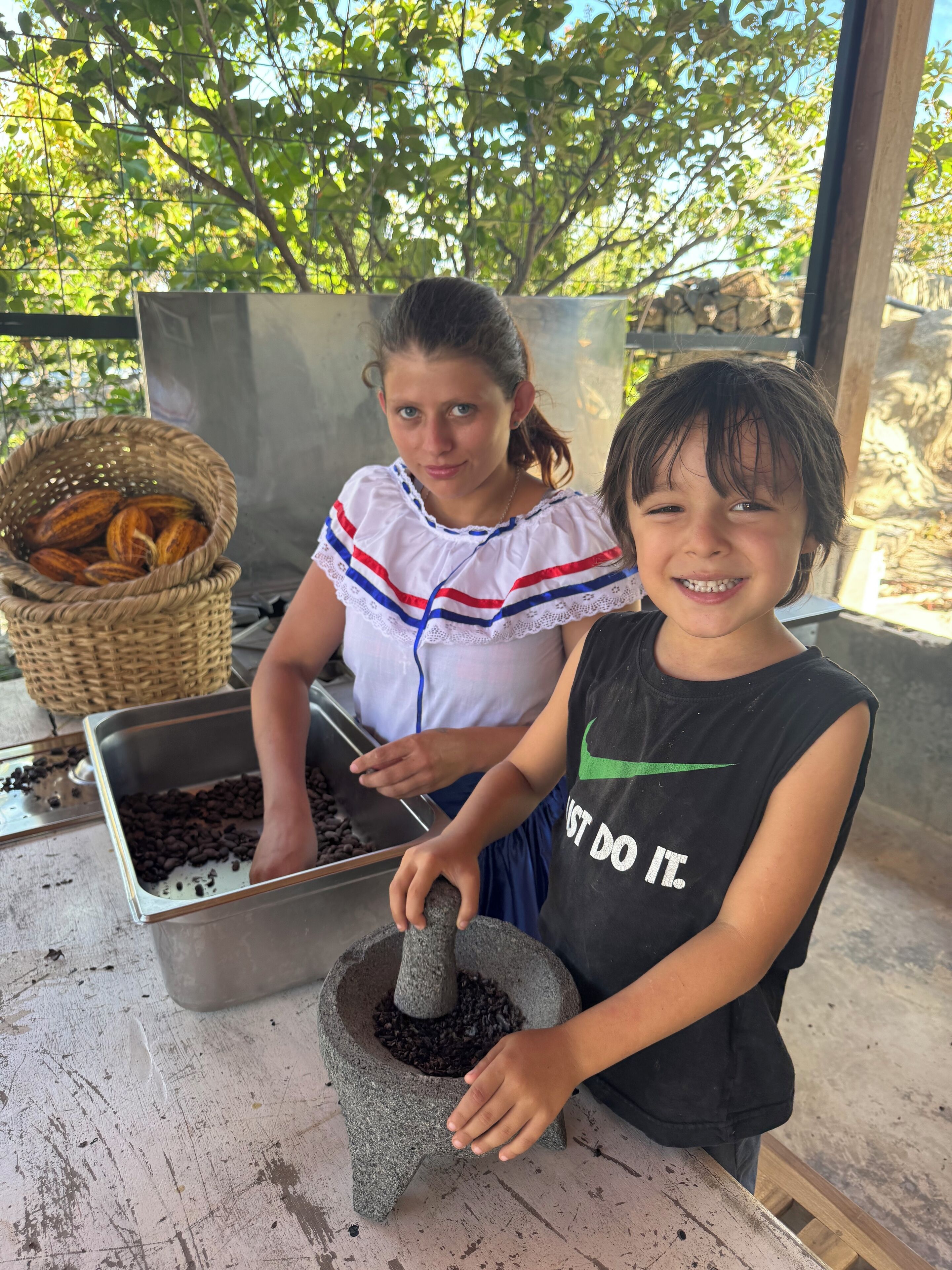Two individuals at a coffee processing station with a stone mill and containers of coffee beans.
