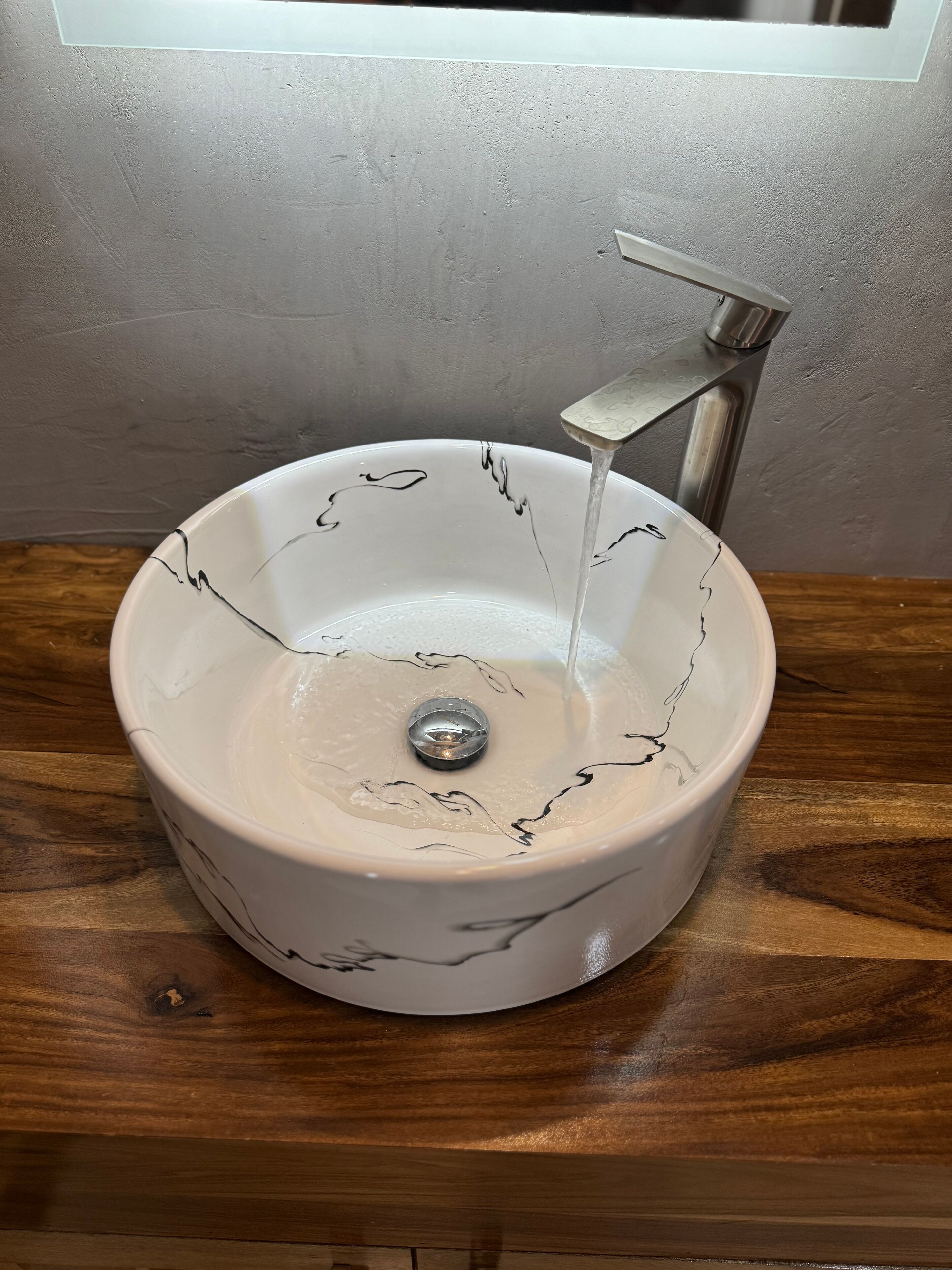 Un lavabo de cerámica blanca con líneas decorativas negras, sobre una encimera de madera.