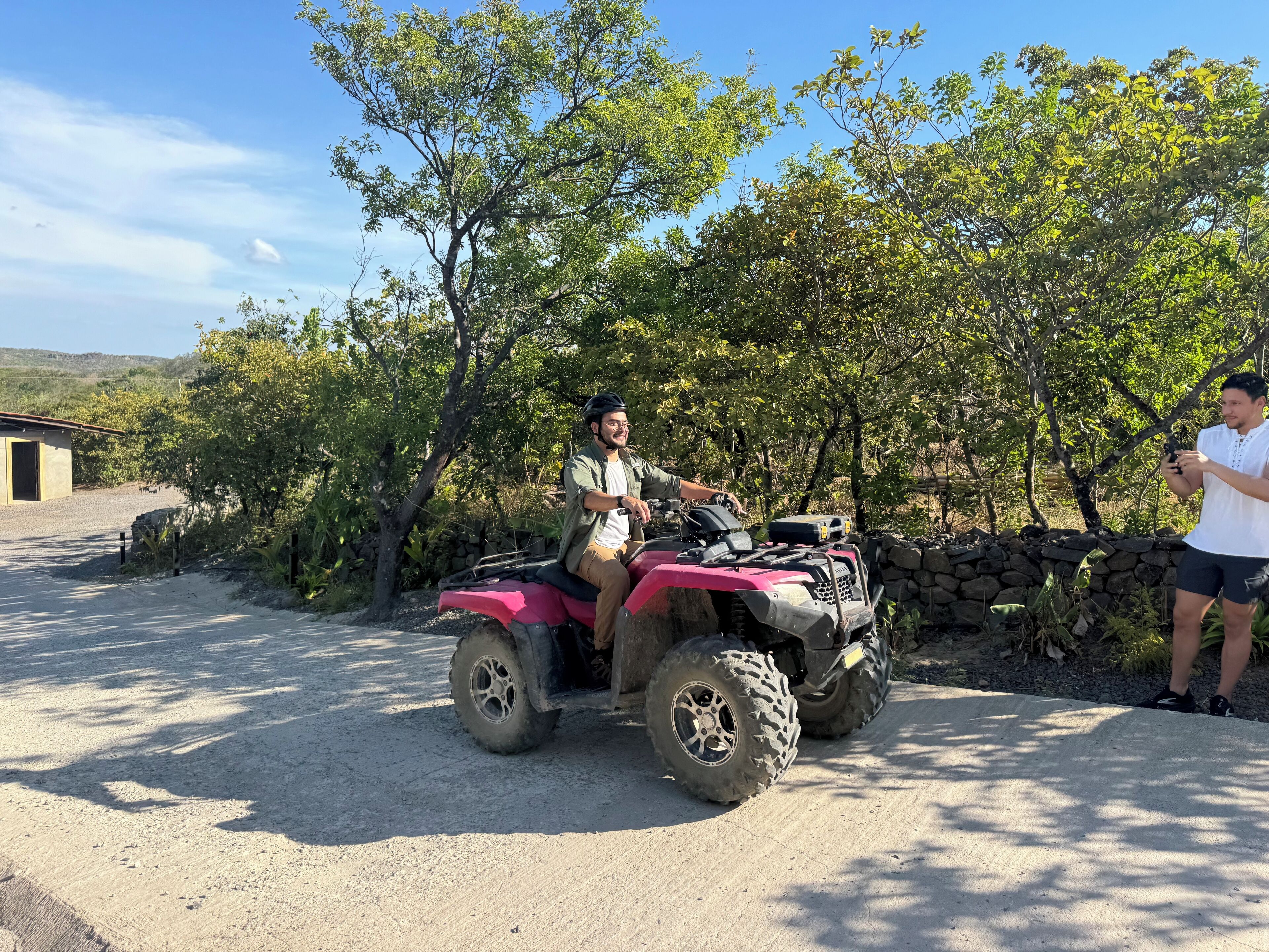 A person riding an ATV on a gravel path with trees and a stone wall in the background.