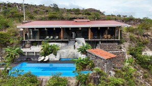 Une maison à deux étages, avec un toit recouvert de tuiles rouges, une piscine et un escalier en pierre menant à une terrasse.