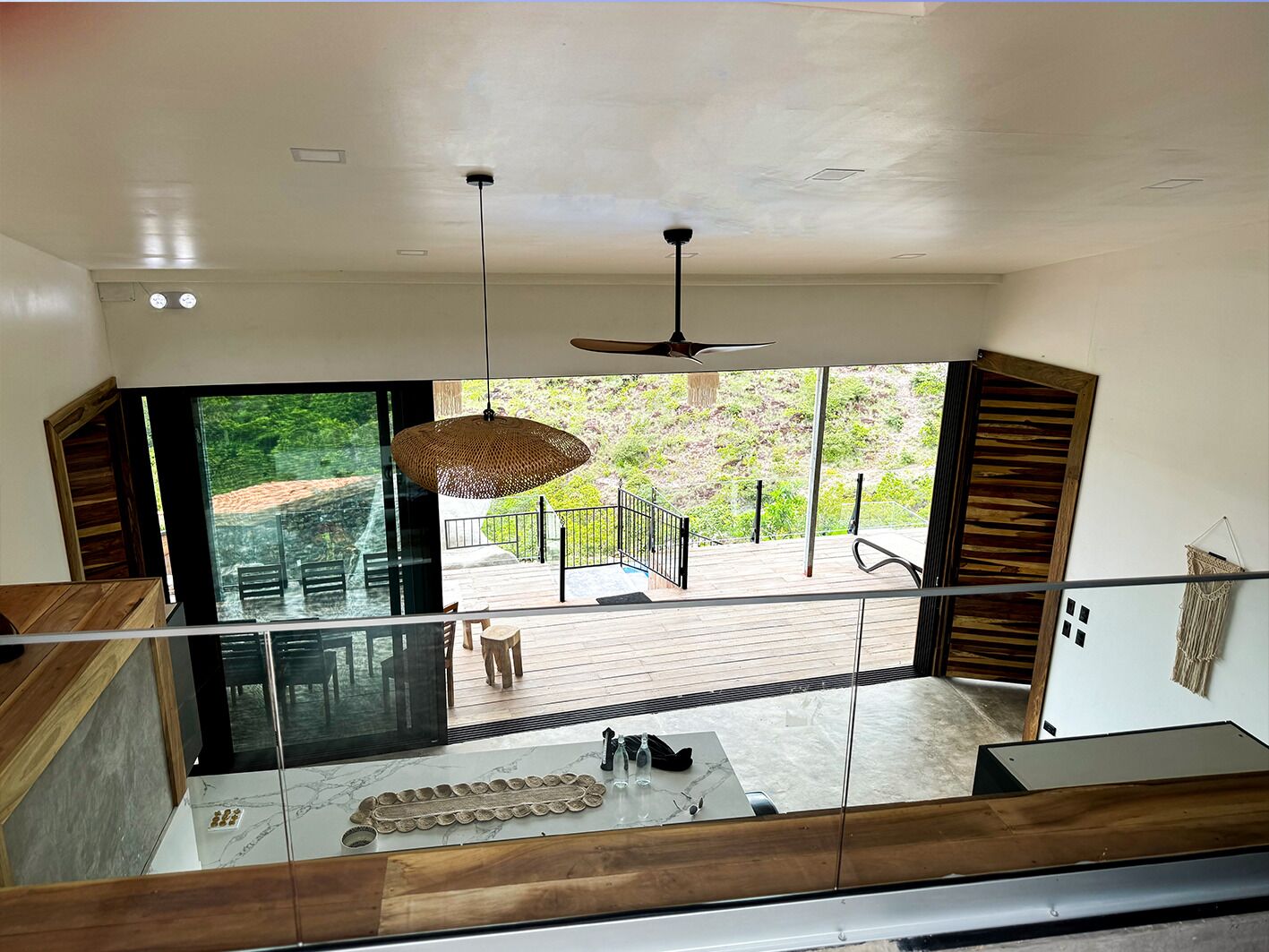 Un interior moderno con un gran ventanal que da a una terraza exterior, una lámpara colgante y un banco de madera.