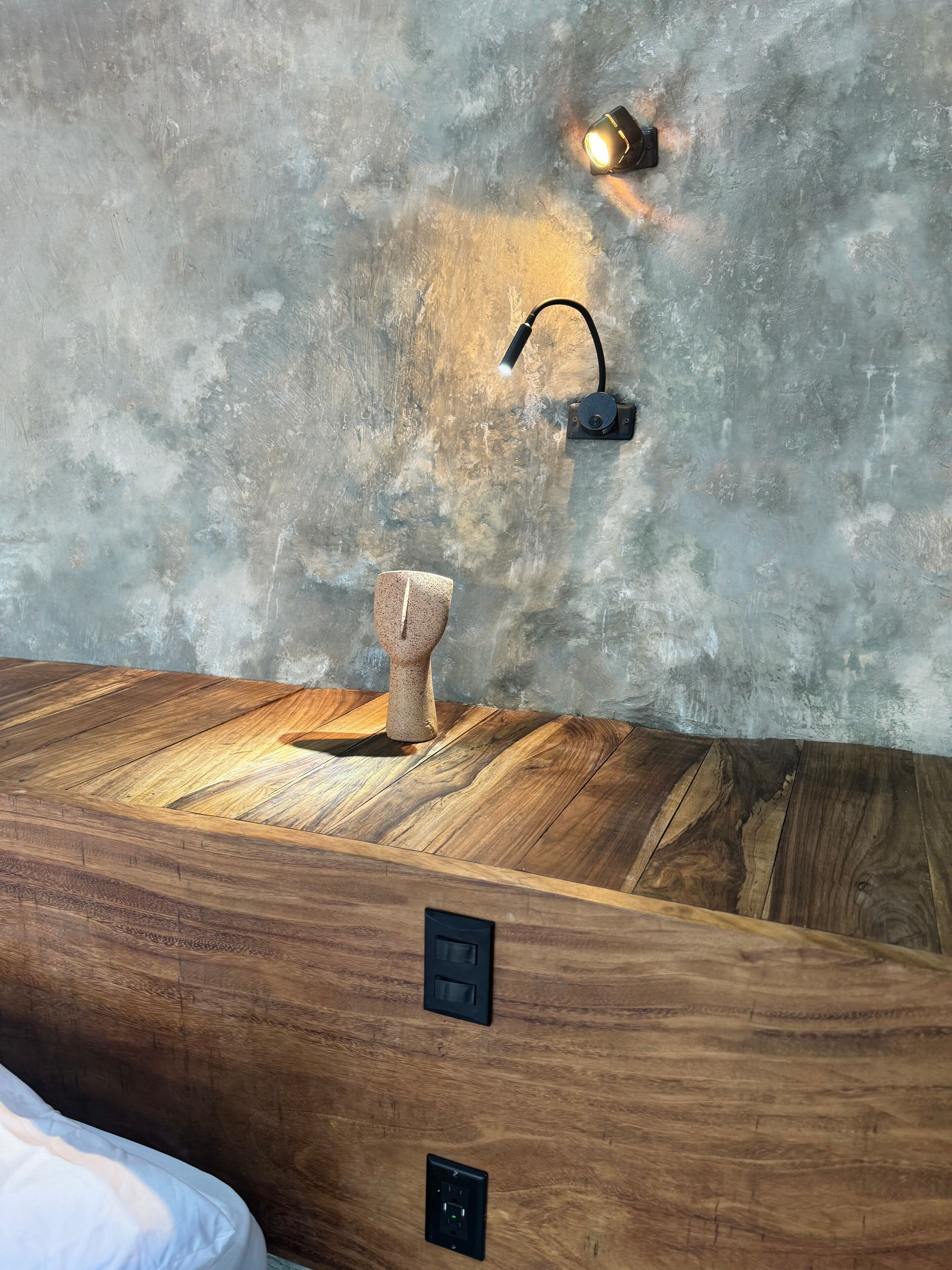 A wooden vanity with a mirror, a towel holder, and a wall-mounted light fixture.