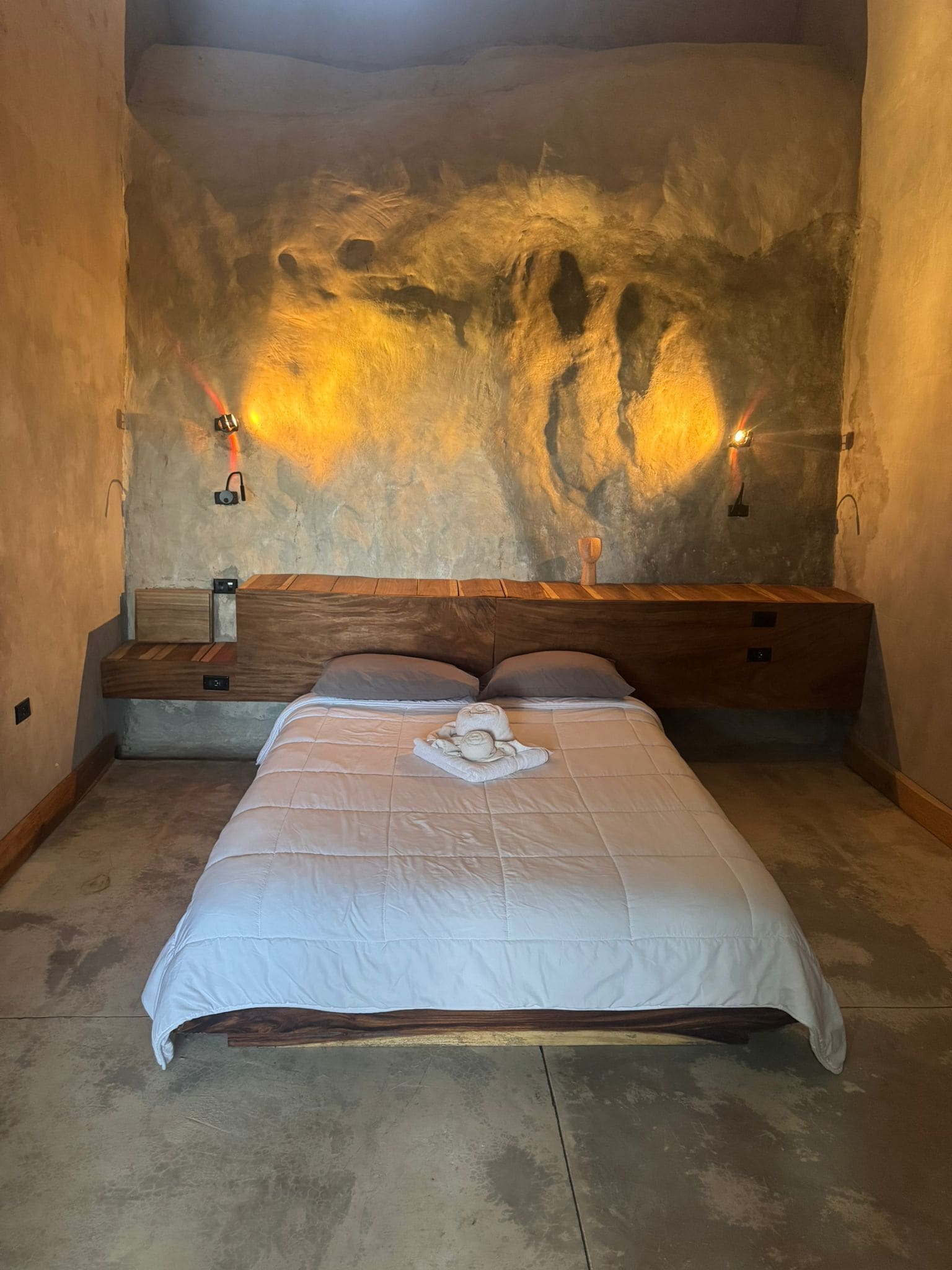A bedroom with a large bed, a wooden headboard, and a textured wall.