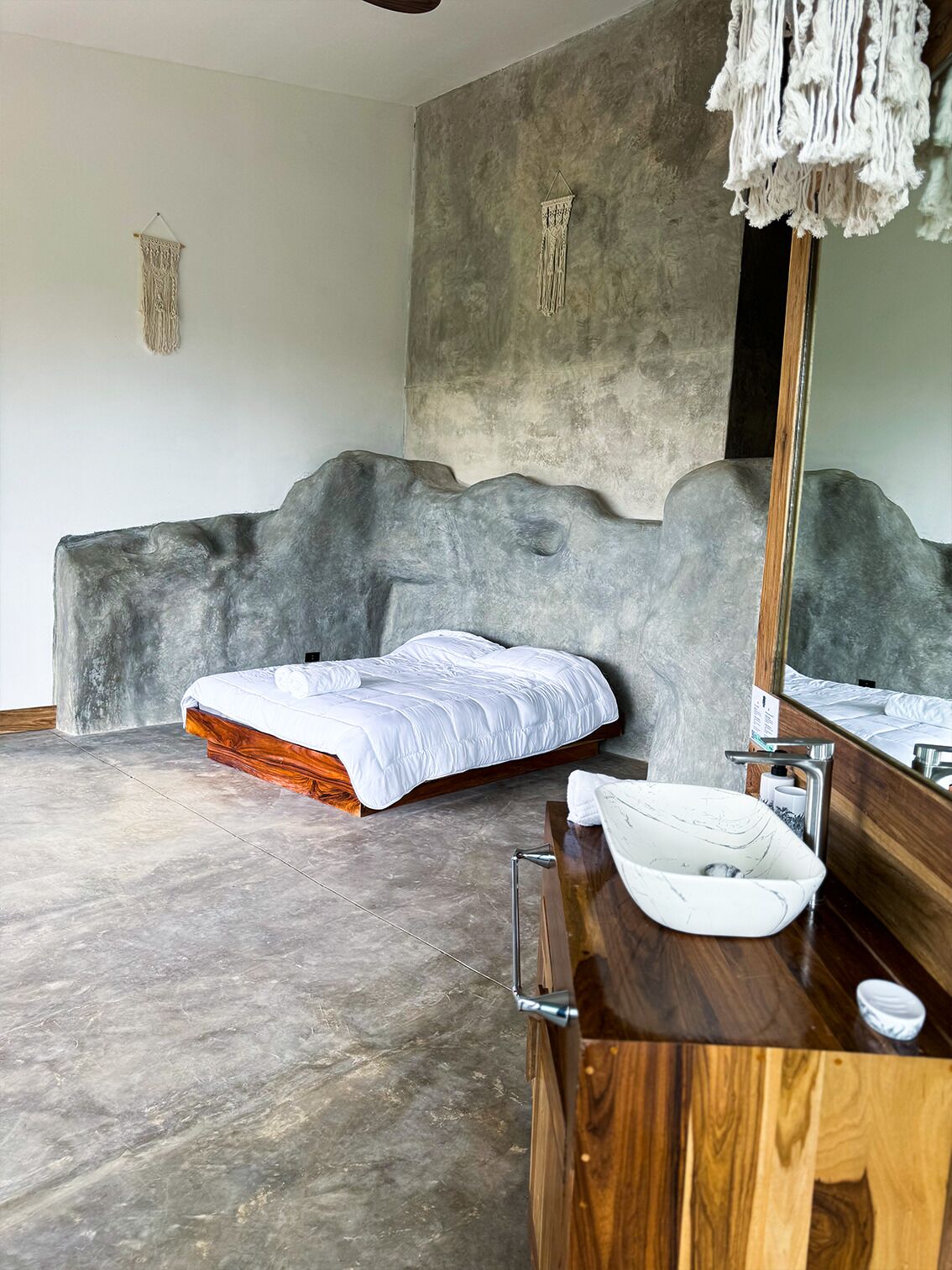 A modern bedroom with a large bed, a wooden dresser, a marble sink, and a large mirror.