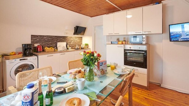 A modern kitchen with a glass dining table, white cabinets, a built-in oven, and a washing machine.