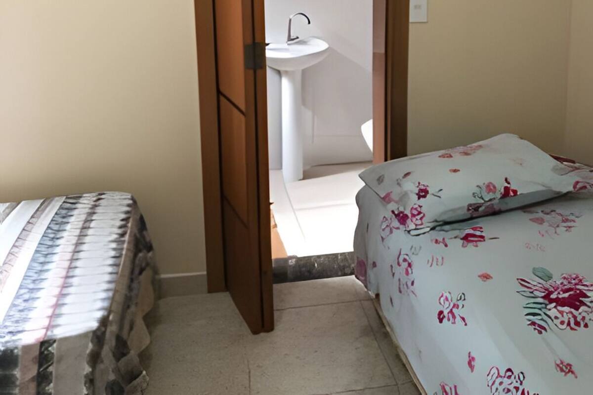 A bedroom with a bed, a floral bedspread, and a view into the bathroom through an open door.