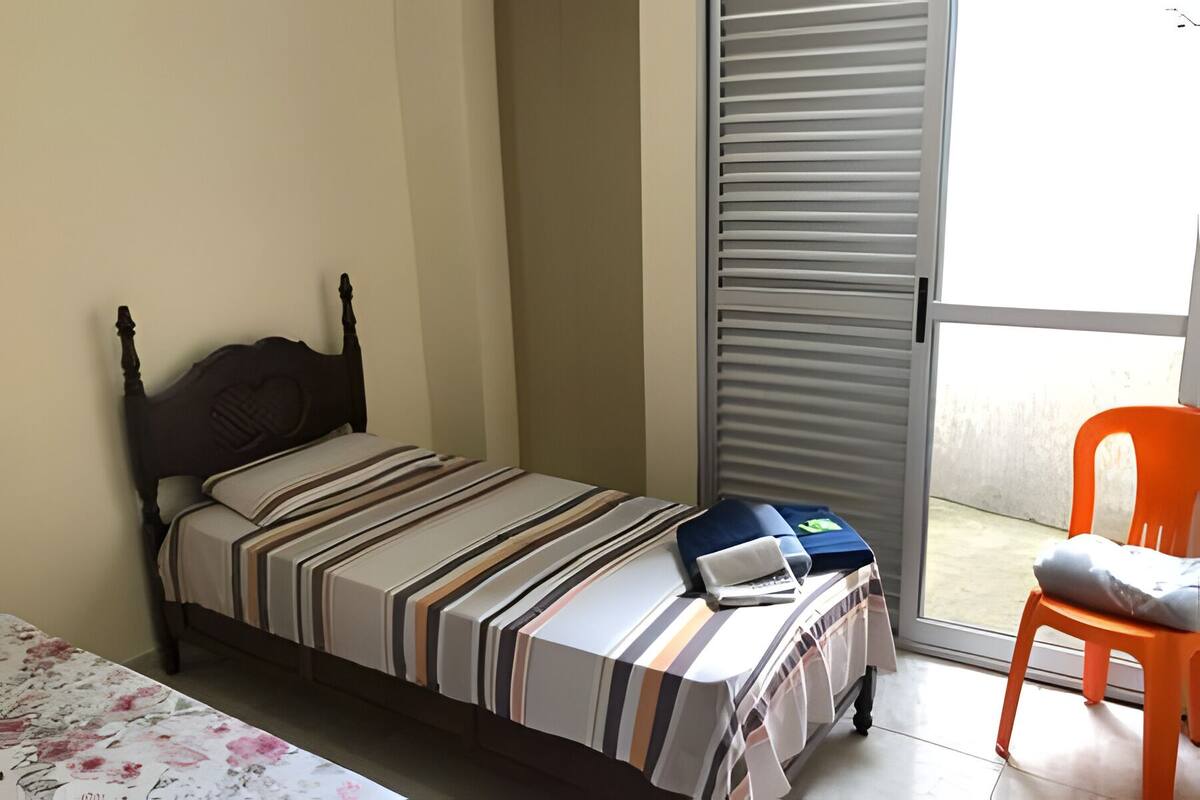 A small bedroom with a bed, a chair, and a sliding door to a balcony.