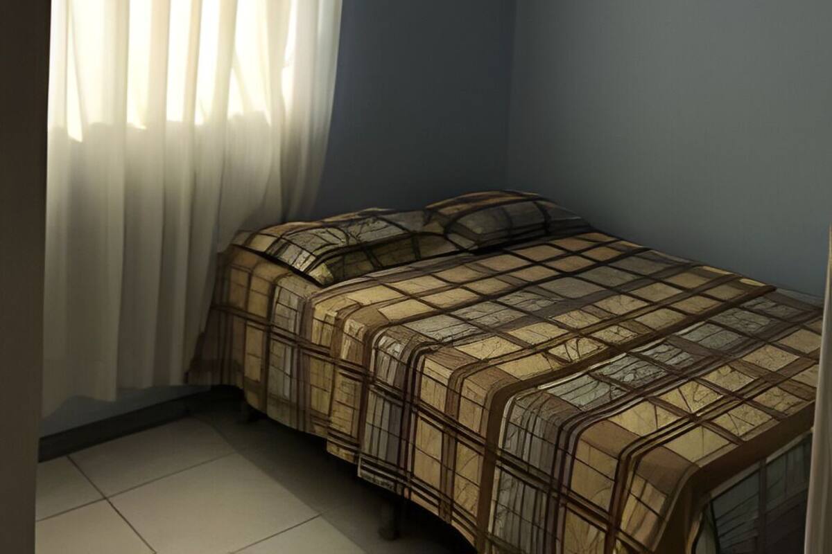 A small, neatly arranged bedroom with a bed, a window with sheer curtains, and a ceiling light.