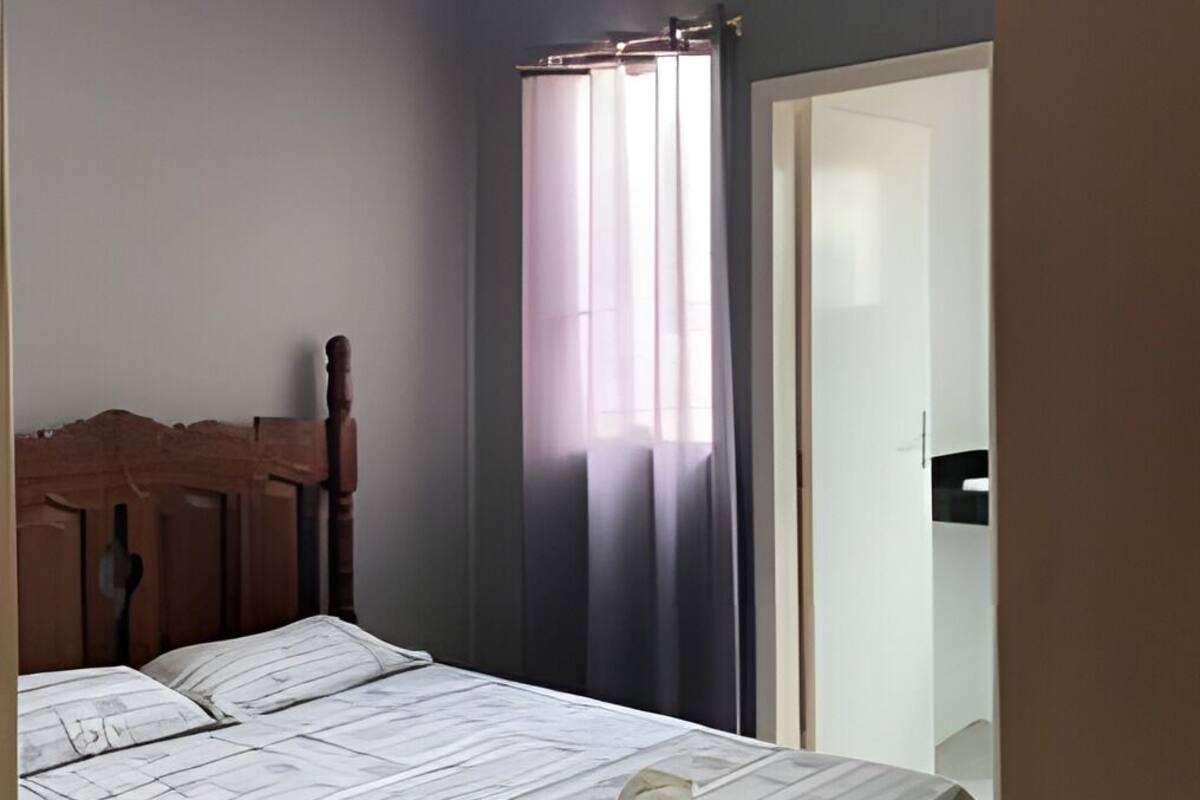 A bedroom with a bed, a wooden headboard, a window with curtains, and a door.