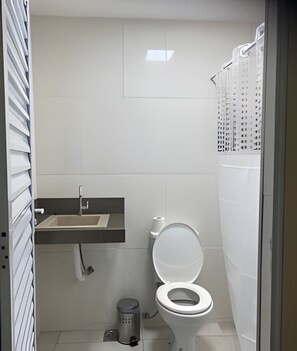 A small, modern bathroom with a toilet, sink, and shower curtain. - NPousadas (Belo Horizonte)