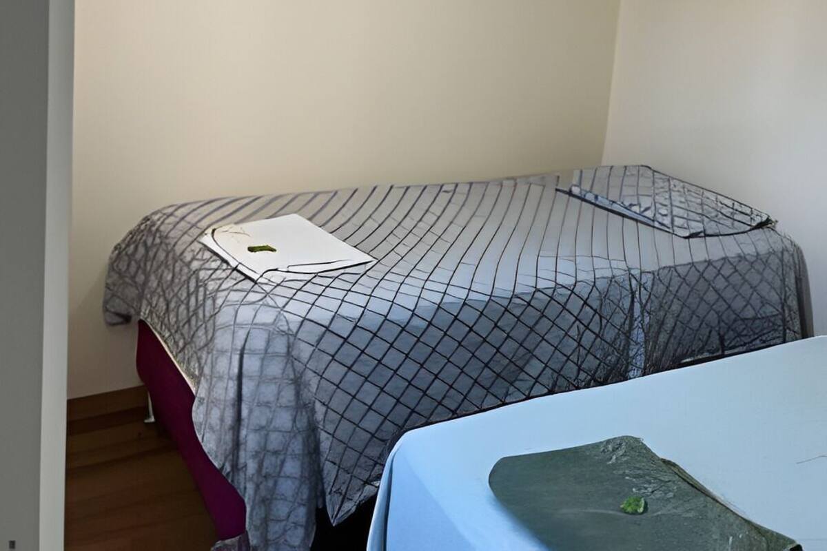 A small, single-bed room with a ceiling fan, a bed with a patterned bedspread, and a small table with a green object on it.