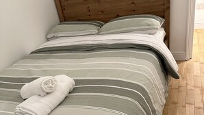 A bed with a wooden headboard, grey and white striped bedding, and a rolled white towel on the footboard.