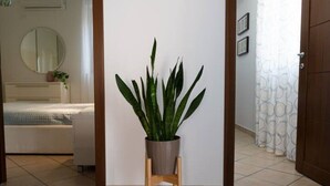 Um corredor com uma planta em vaso sobre um suporte de madeira, um espelho na parede e uma porta com cortinas estampadas.