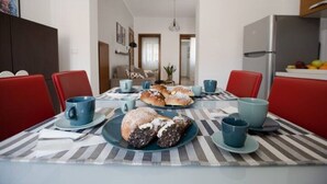 Uma sala de jantar com mesa posta para quatro pessoas, com toalha listrada, xícaras azuis e pratos com doces.